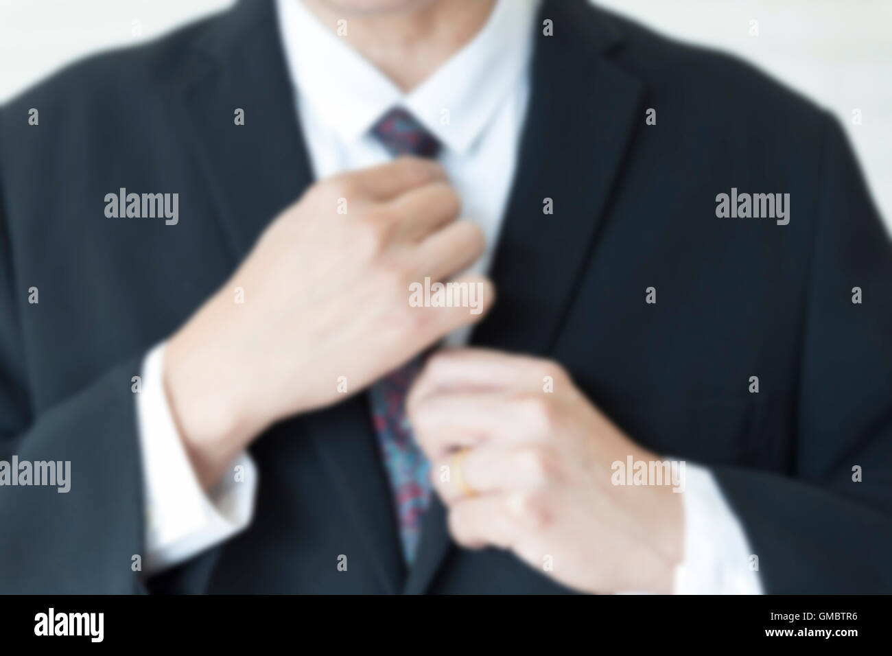 Homme d'affaires en costume noir organiser sa cravate - flou pour utiliser comme arrière-plan Banque D'Images