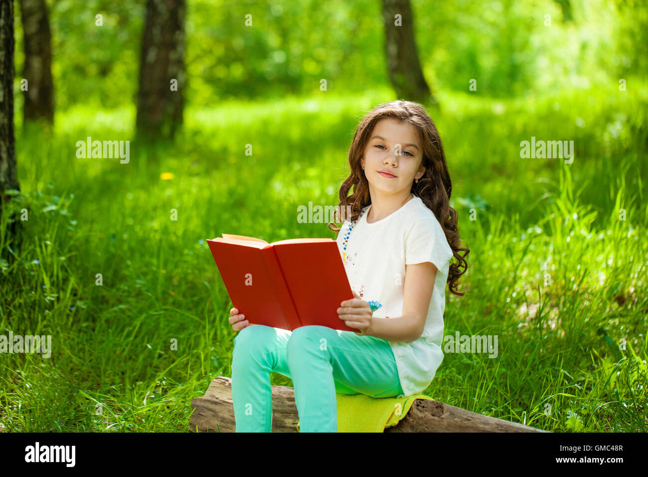 Charmante petite fille en forêt avec livre sur l'arrière-plan de parc d'été Banque D'Images