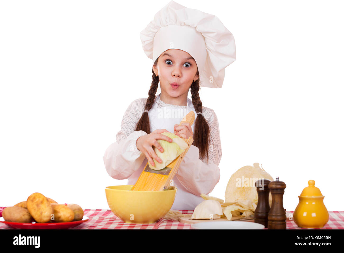 Portrait d'une petite fille dans un tablier blanc et chefs hat râper le chou dans la cuisine, isolé sur fond blanc Banque D'Images