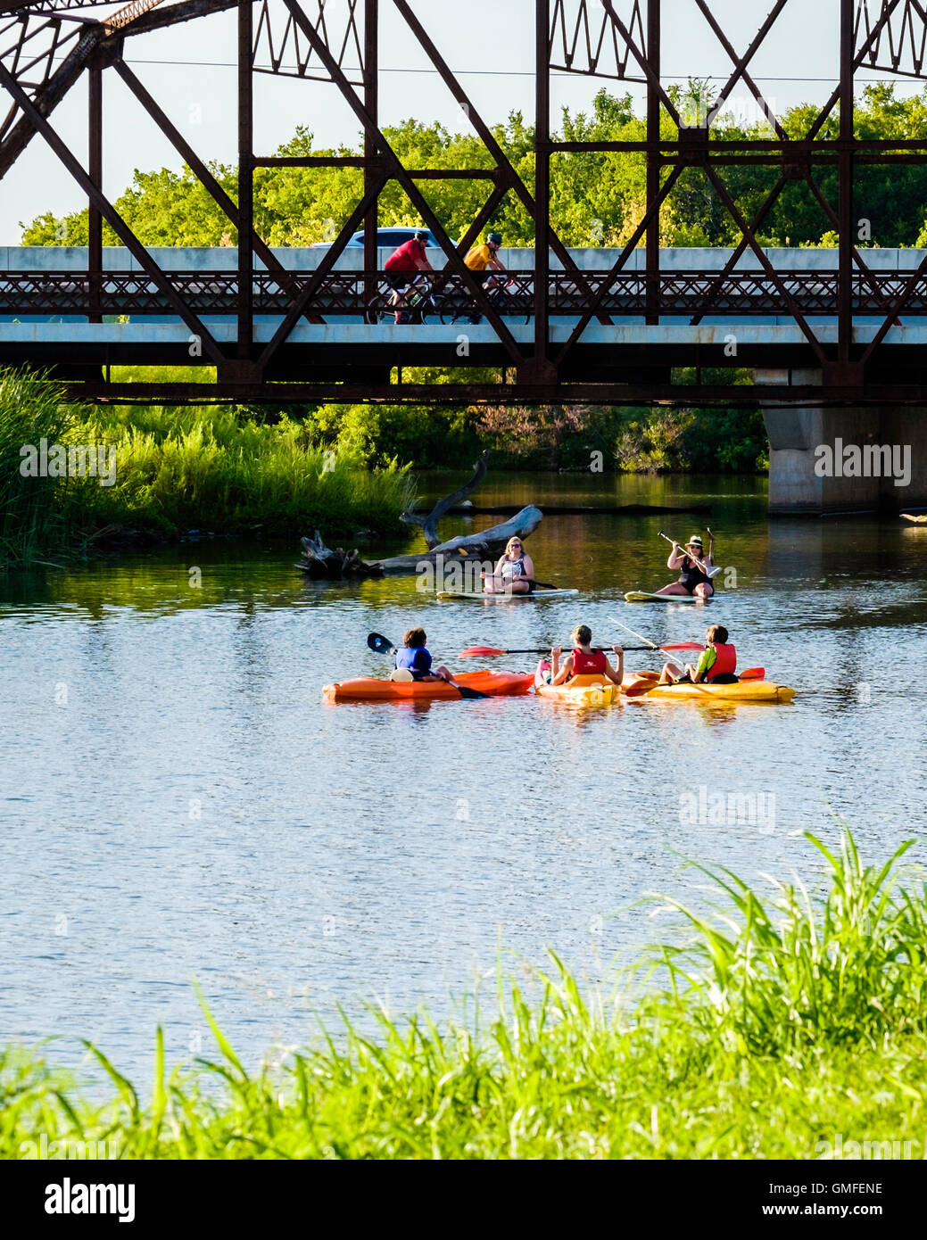 Deux femmes s'asseoir sur paddleboards tandis que 3 garçons paddle petit kayaks sous un vieux pont en treillis en acier sur la route 66. North Canadian river, New York, USA. Banque D'Images
