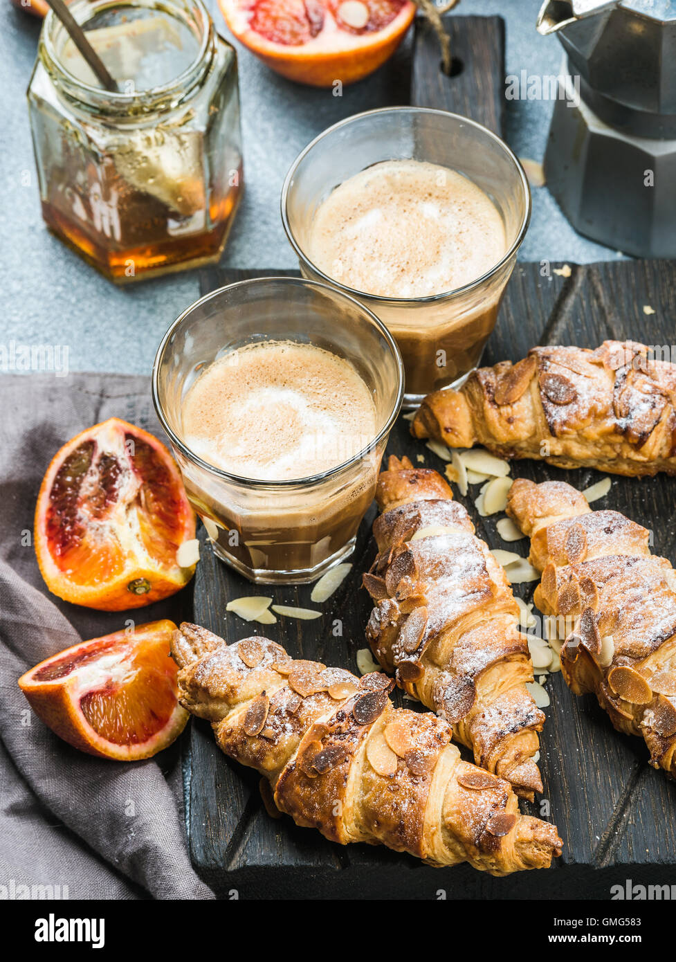Petit-déjeuner maison traditionnelle de style italien. Latte dans les verres, des croissants aux amandes et oranges siciliennes sanglant rouge sur tableau texturé en béton Banque D'Images