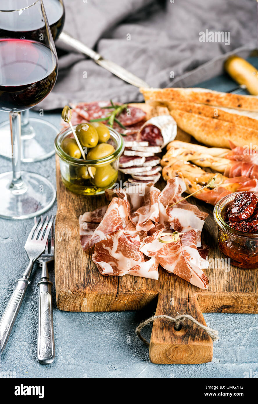 Sélection de hors-d'la viande. Salami, prosciutto, bâtonnets de pain, baguette, olives et tomates séchées, deux verres de vin rouge sur fond texturé de béton gris Banque D'Images