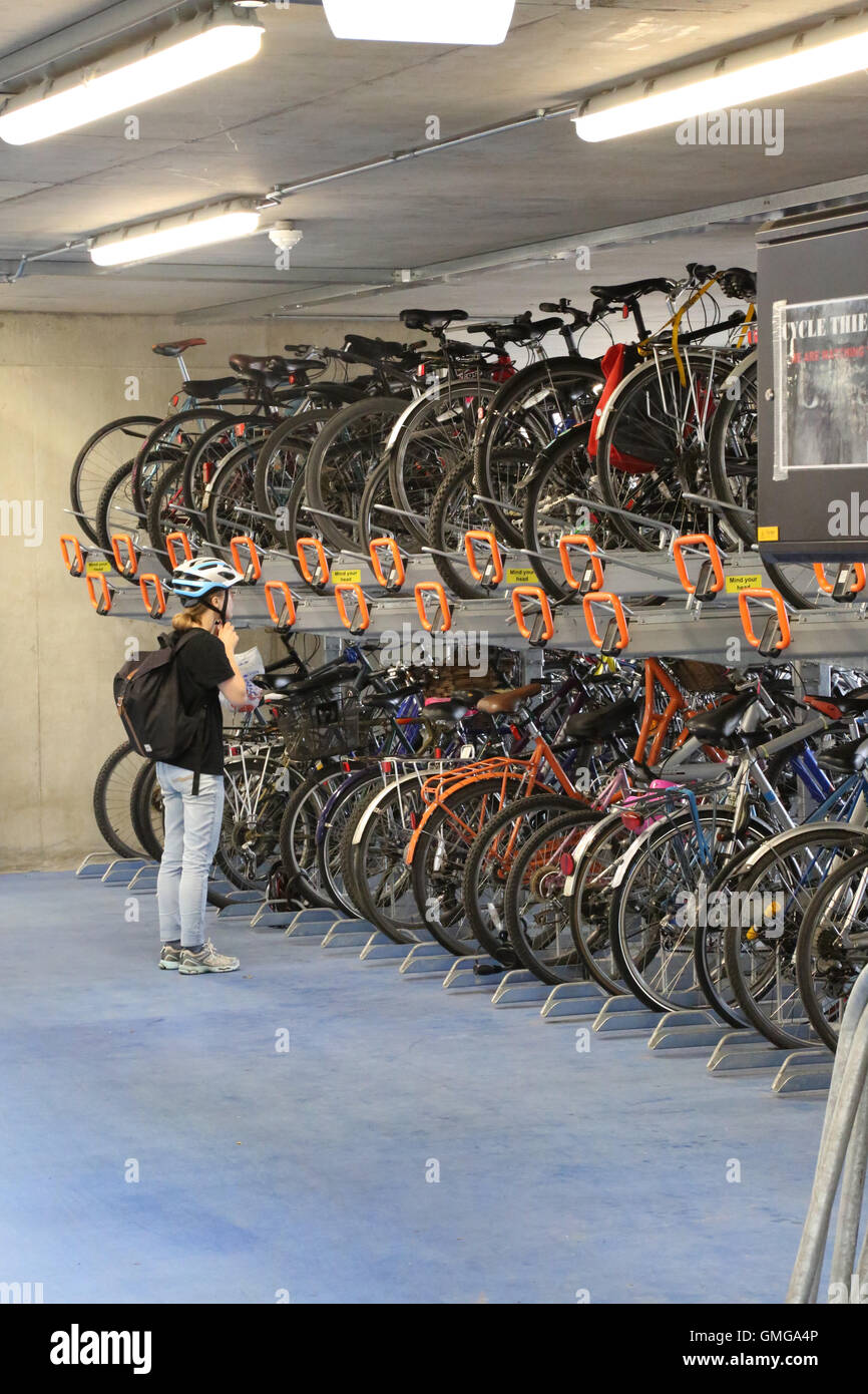 Un cycliste ajuste son chapeau avant de déposer son vélo à partir de la grille d'une nouvelle histoire du parc à vélos à Cambridge, Royaume-Uni. Banque D'Images