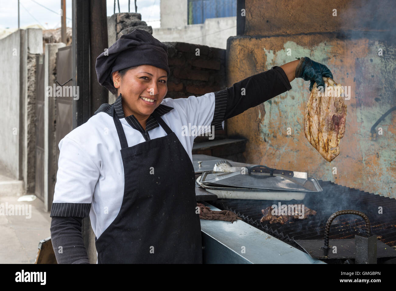 Une femme cuisinière montrant un morceau de viande qu'elle est sur le point de mettre sur un grill. Quito, Equateur. Banque D'Images