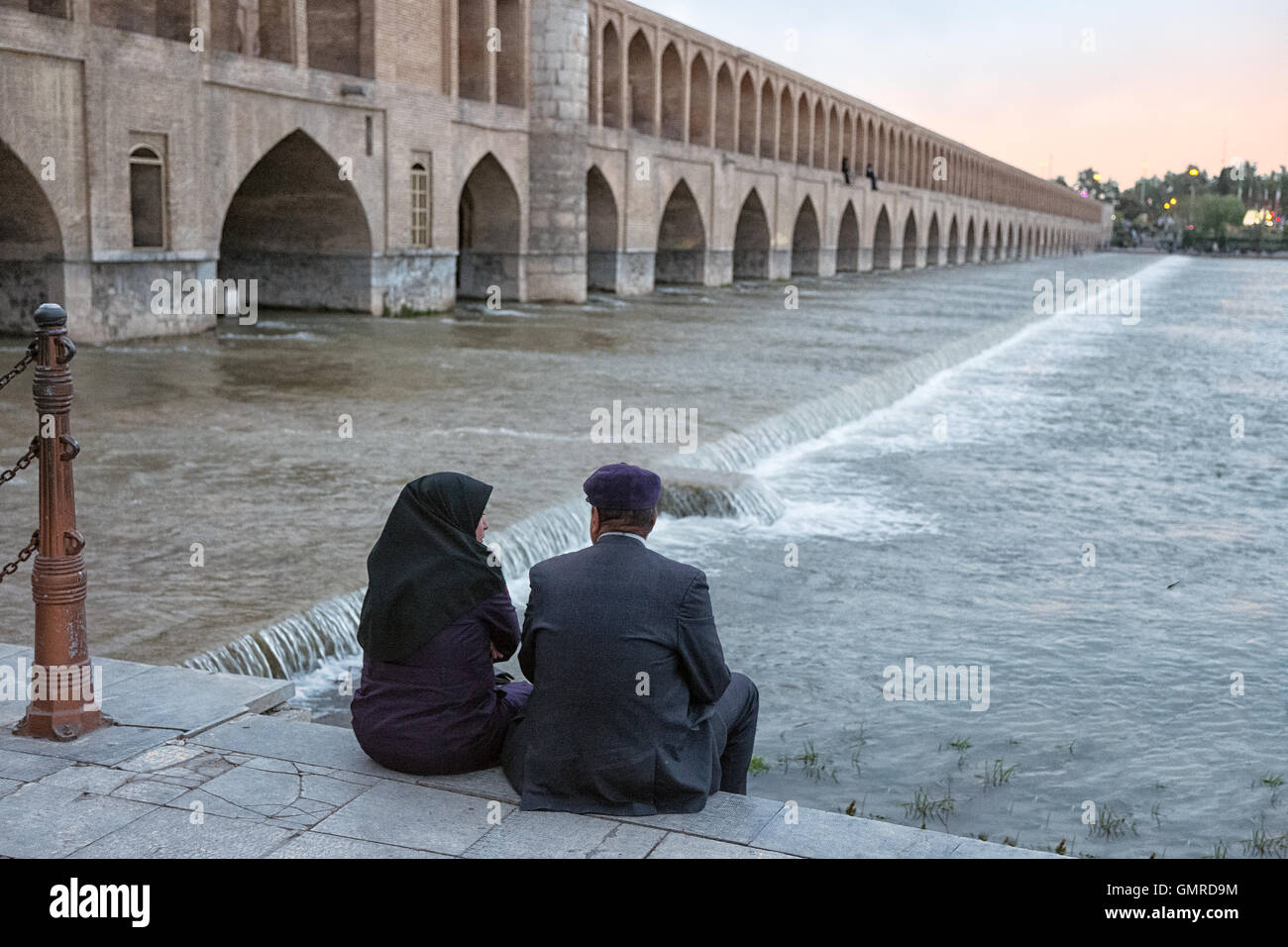 Couple iranien assis sur les rives de la rivière Zayandeh. Allāhverdi Khan populairement connu sous le nom de pont Si-O-seh pol "Le pont de trente-trois travées" est l'un des 11 ponts d'Isfahan, Iran et le plus long pont sur la rivière Zayandeh avec la longueur totale de 297,76 mètres (976,9 pieds). Il est hautement classé comme étant l'un des exemples les plus célèbres de la conception de ponts safavides. Banque D'Images