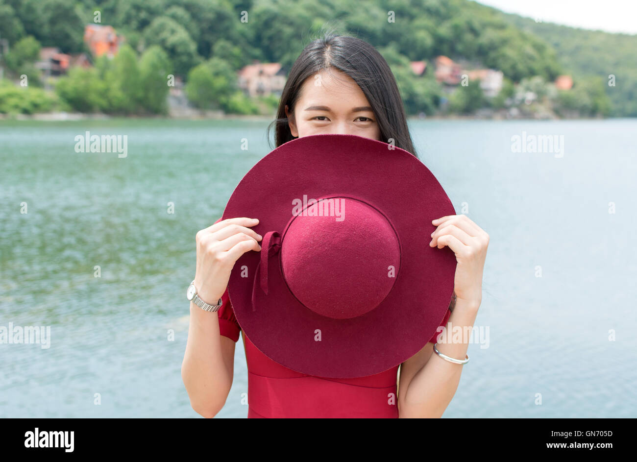 Mode femme holding hat standing in front of a lake Banque D'Images