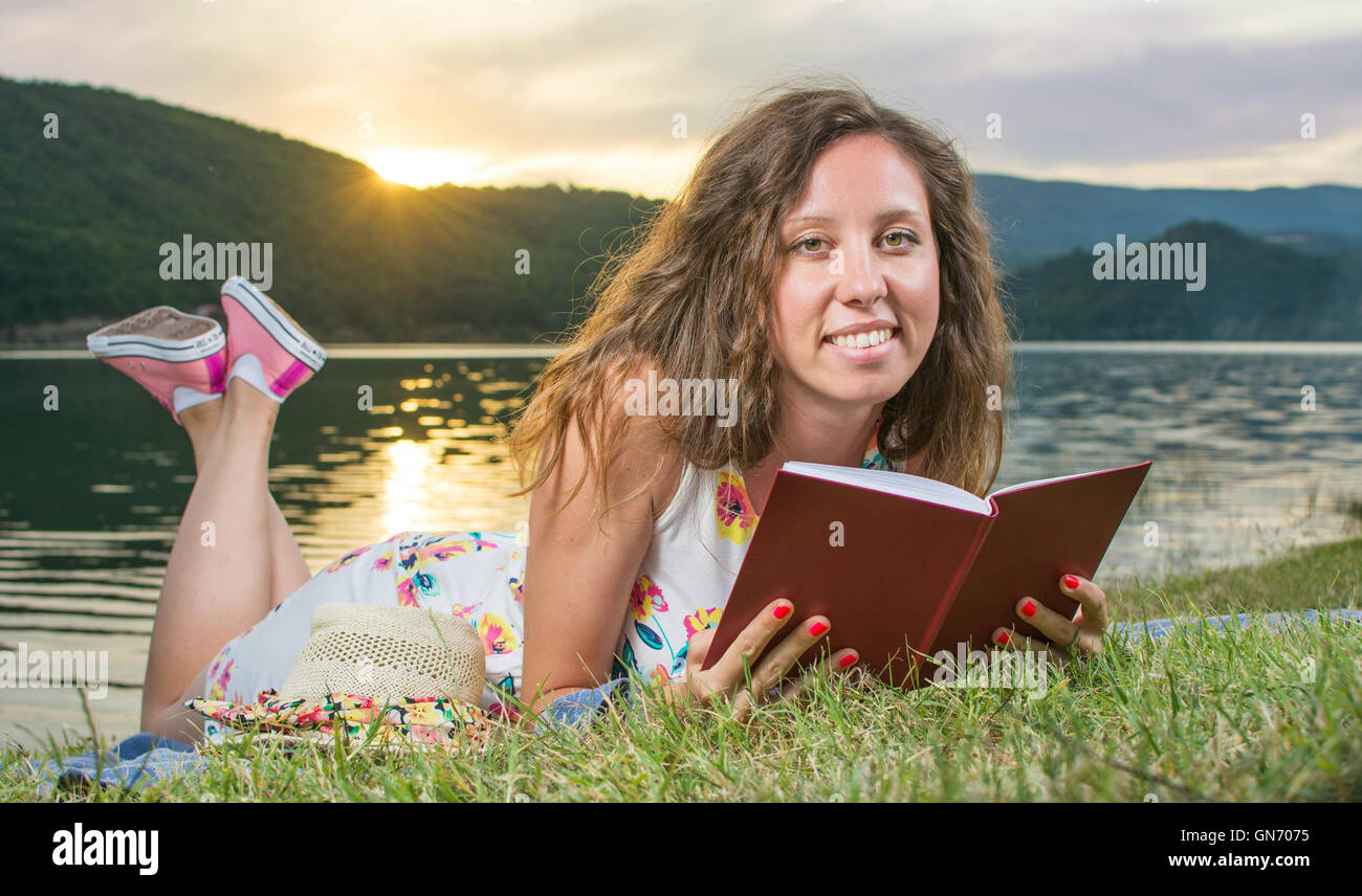 Jeune femme lisant un livre par le lac. Relaxation Solo Banque D'Images