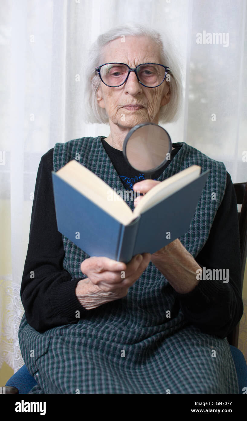 Quatre-vingt-dix ans grand-mère la lecture d'un livre par loupe Banque D'Images
