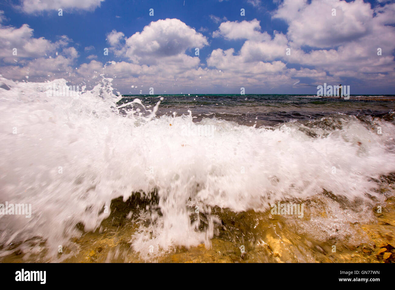 Pêcheur solitaire à marée basse sur une plage d'une vague se brise sur la rive à l'avant-plan Banque D'Images