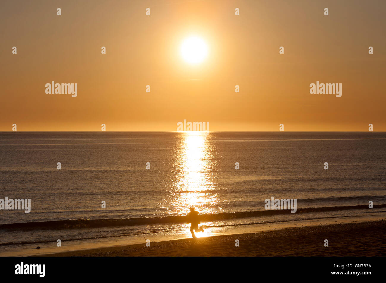 Un coucher de soleil sur l'océan et une silhouette d'une personne qui marche sur la plage. Banque D'Images