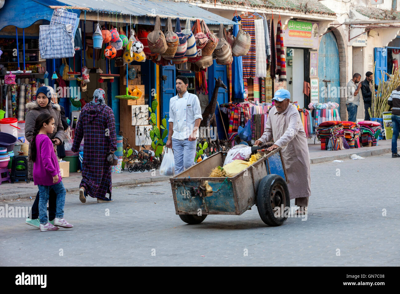 Essaouira, Maroc. Porter poussant le panier avec les achats du shopping dans l'Avenue de l'Istiqlal. Banque D'Images