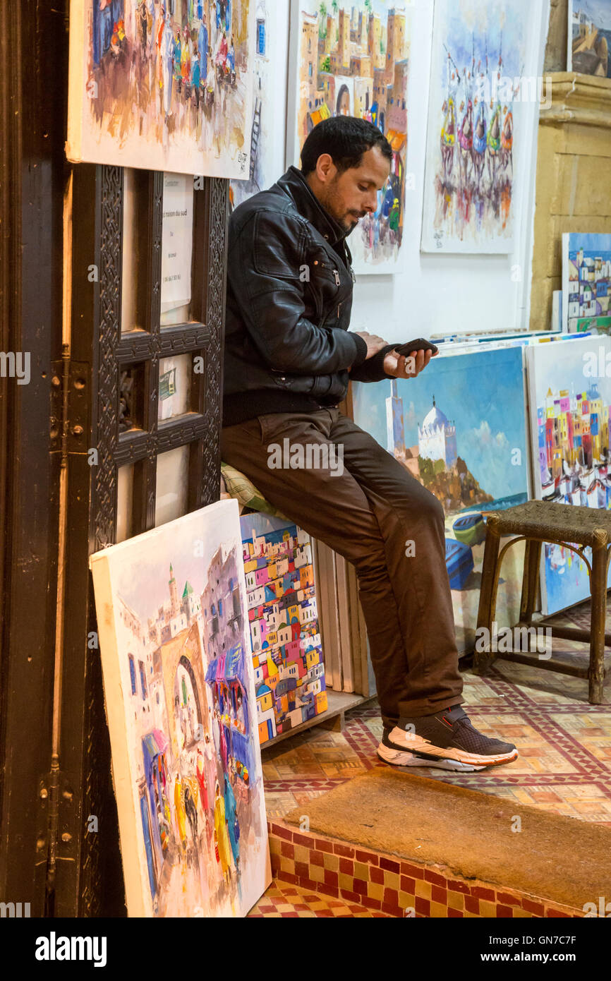 Essaouira, Maroc. Art Gallery Greffier vérifie son téléphone cellulaire. Banque D'Images