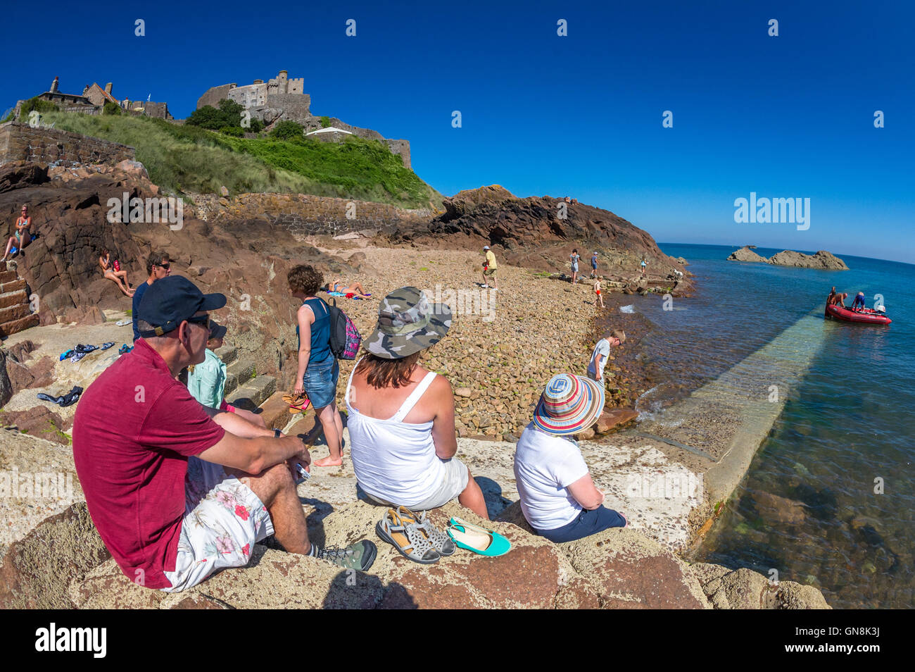 Les vacanciers s'asseoir sur des mesures concrètes à Gorey Harbour avec château Mont Orgueil en arrière-plan, New Jersey. Banque D'Images