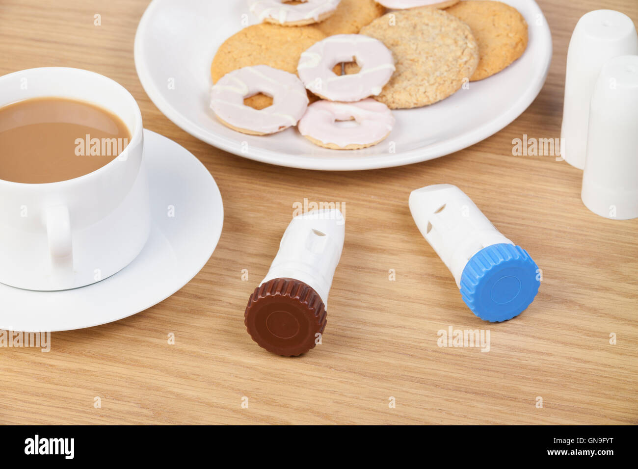 Brun et bleu asthme inhalateurs à poudre portant sur la table du petit déjeuner à côté d'une tasse de café et une assiette de biscuits Banque D'Images