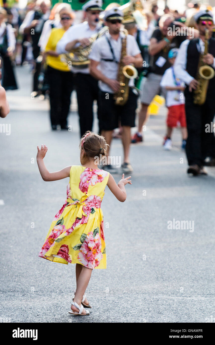 Petite fille, 5-6 ans, de public, faire le pas de l'avant du défilé et de la danse, volé la vedette. Parade en arrière-plan s'approcher d'enfant. Banque D'Images