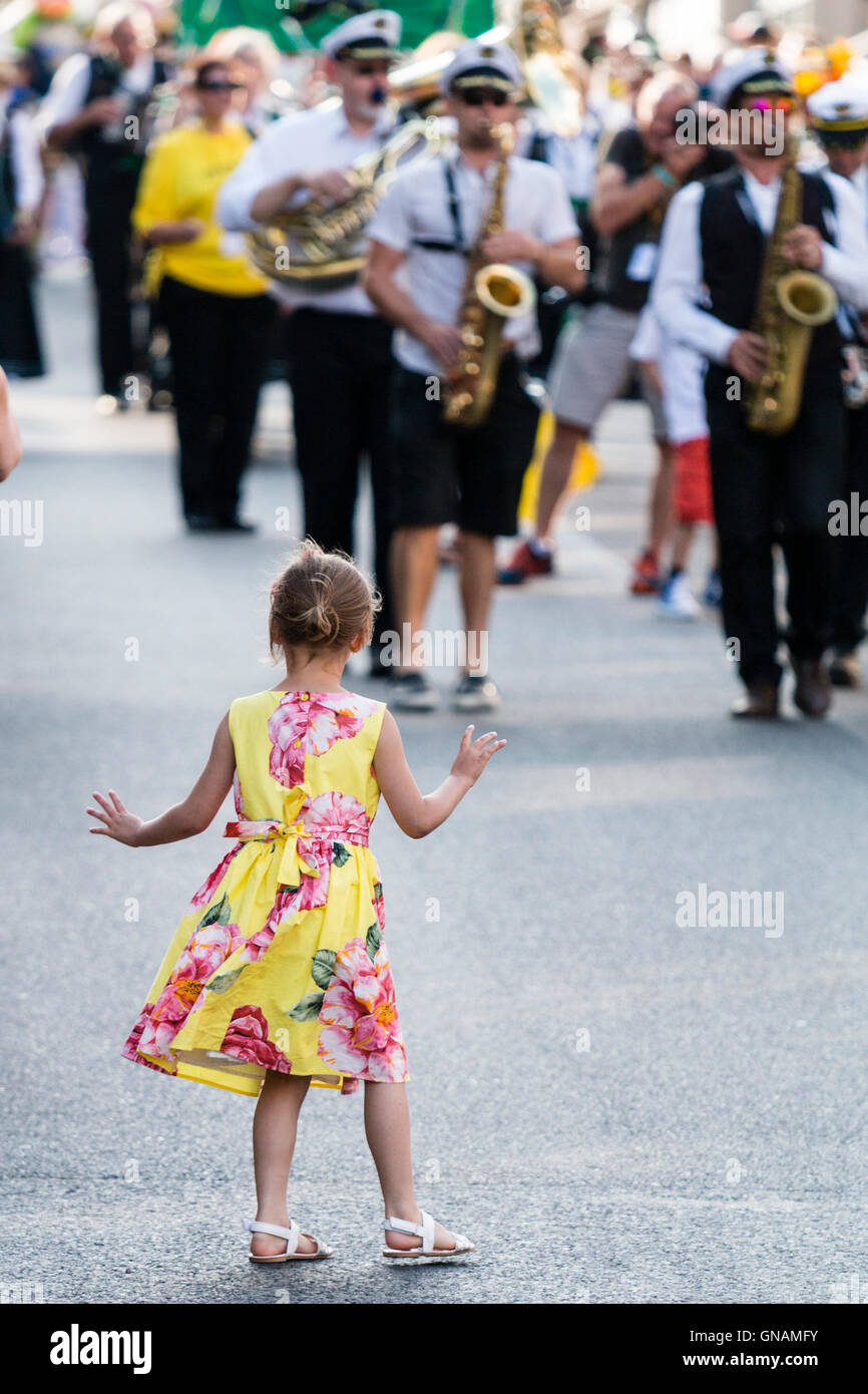 Petite fille, 5-6 ans, de public, faire le pas de l'avant du défilé et de la danse, volé la vedette. Parade en arrière-plan s'approcher d'enfant. Banque D'Images