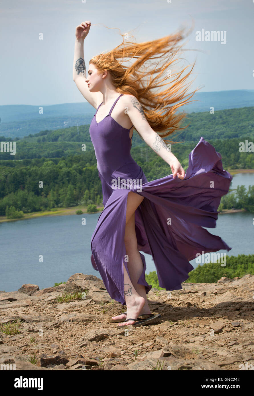 Portrait dramatique de belle tête rouge femme en robe pourpre, en montagne avec le vent dans les cheveux et un lac ci-dessous. Banque D'Images