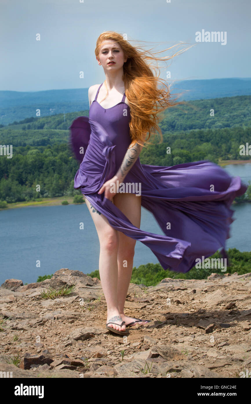 Portrait dramatique de belle tête rouge femme en robe pourpre, en montagne avec le vent dans les cheveux et un lac ci-dessous. Banque D'Images