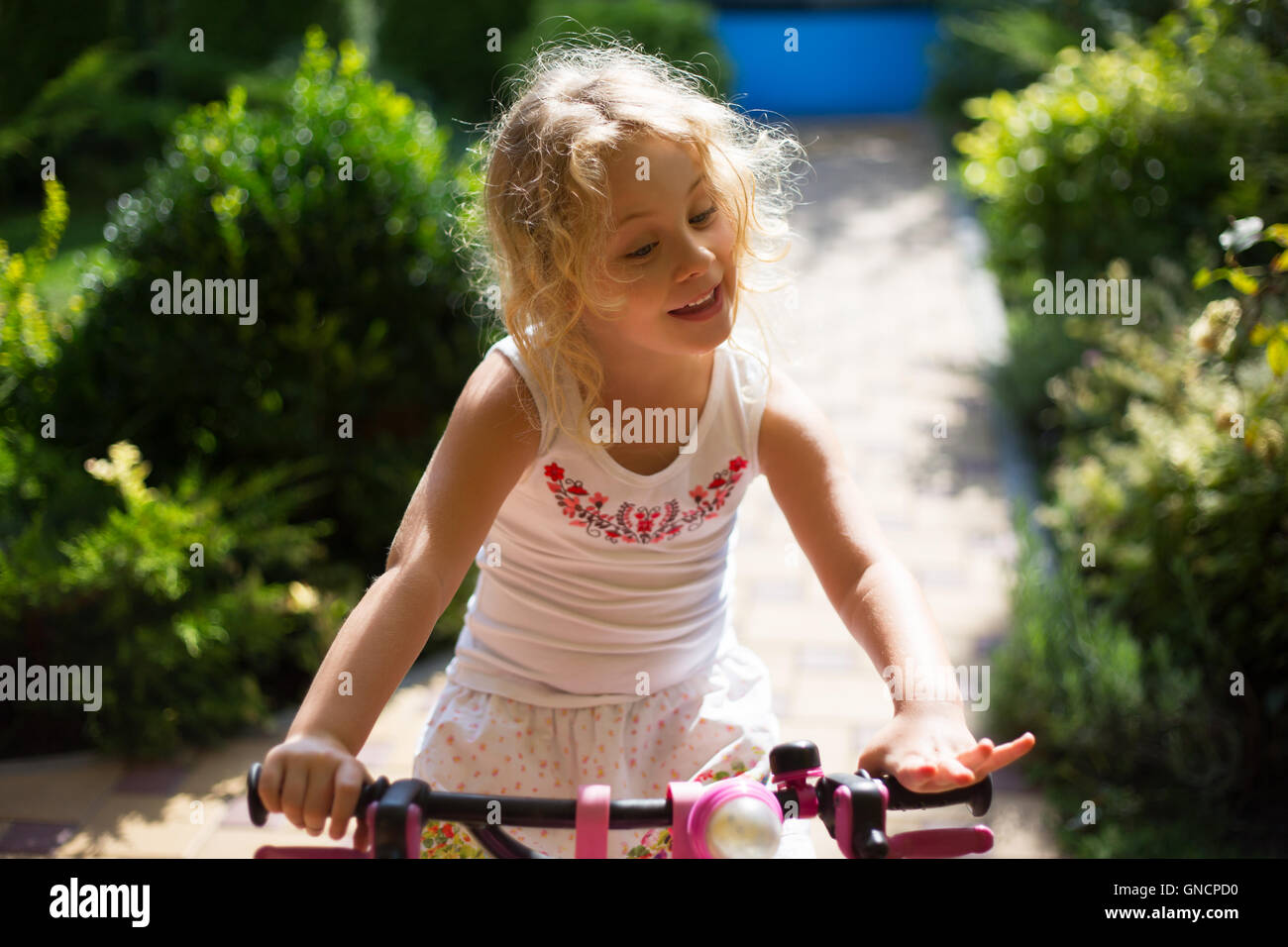 Belle petite fille sur un vélo dans le parc, piscine d'été Banque D'Images