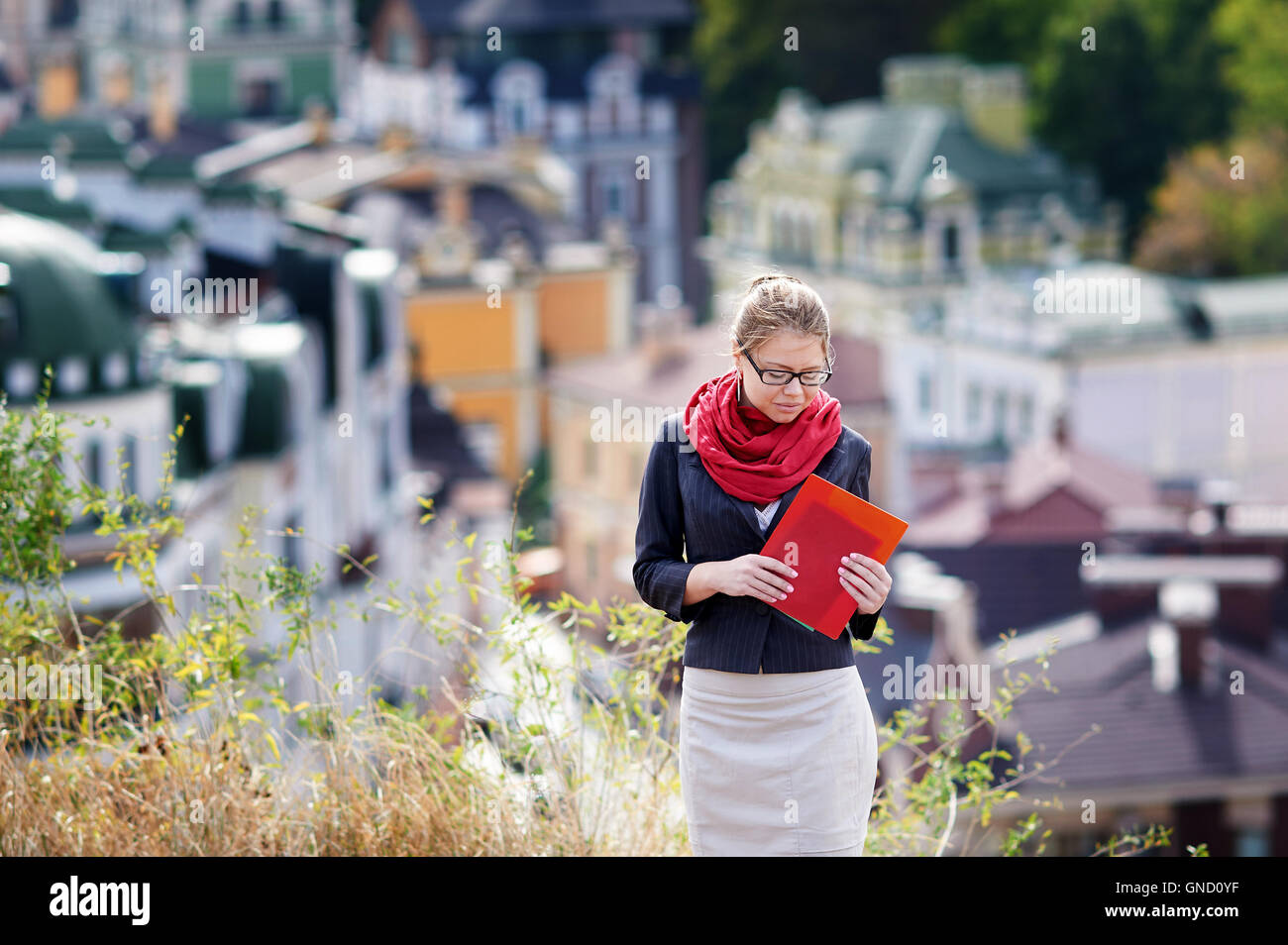 Jeune femme à lunettes avec dossier rouge dans les mains sur fond de la ville Banque D'Images