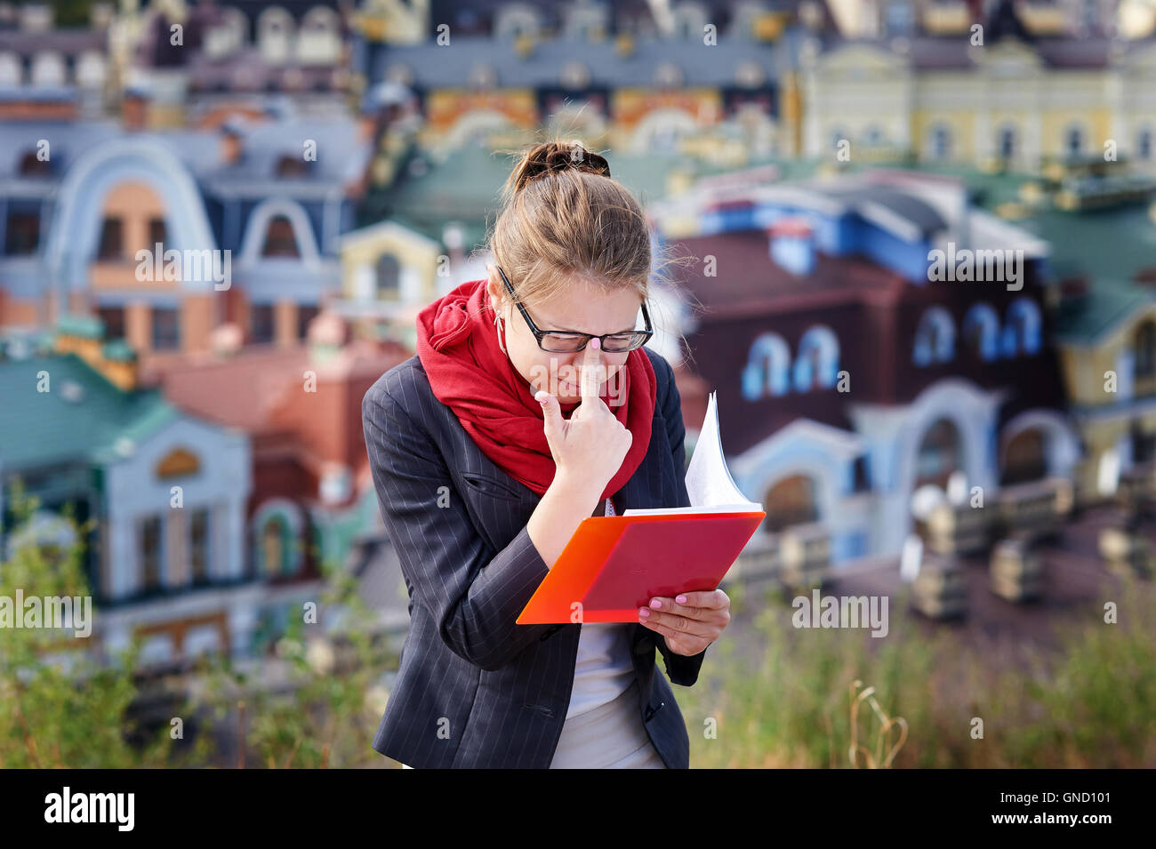 Jeune femme à lunettes avec dossier rouge dans les mains sur fond de la ville Banque D'Images