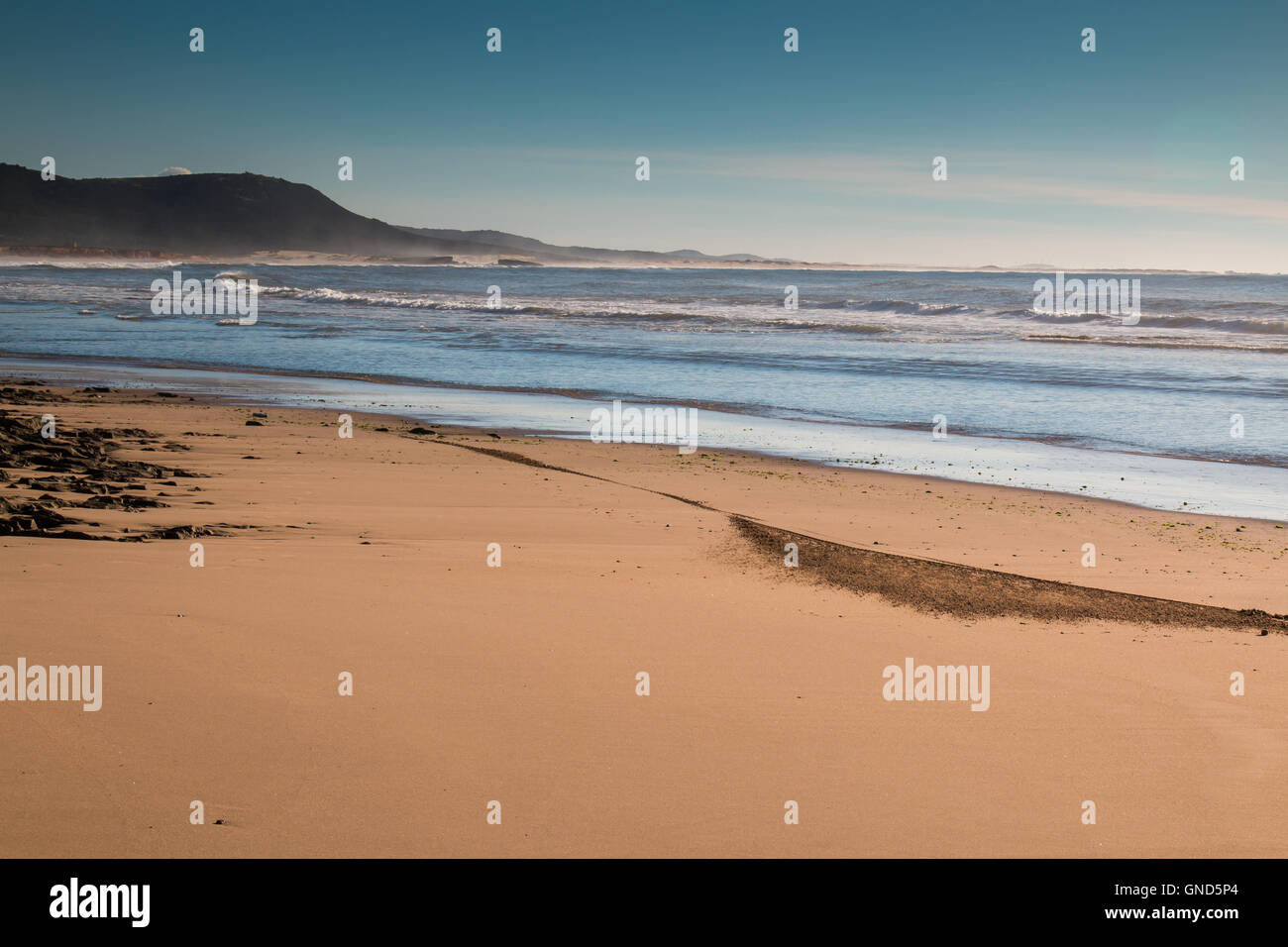 Plage de sable à la côte de l'océan Atlantique au Maroc. Les petites vagues de l'océan. Montagne dans l'arrière-plan. Début de soirée peu c Banque D'Images