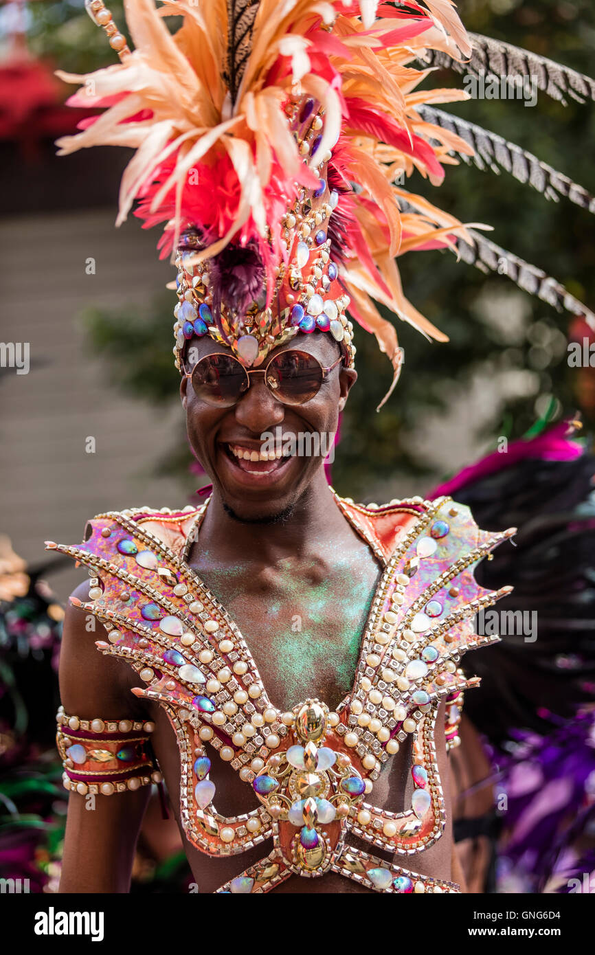 Jolie femme noire avec un sourire rouge et d'orange à la coiffure de plumes du carnaval de Notting Hill dans l'ouest de Londres Banque D'Images