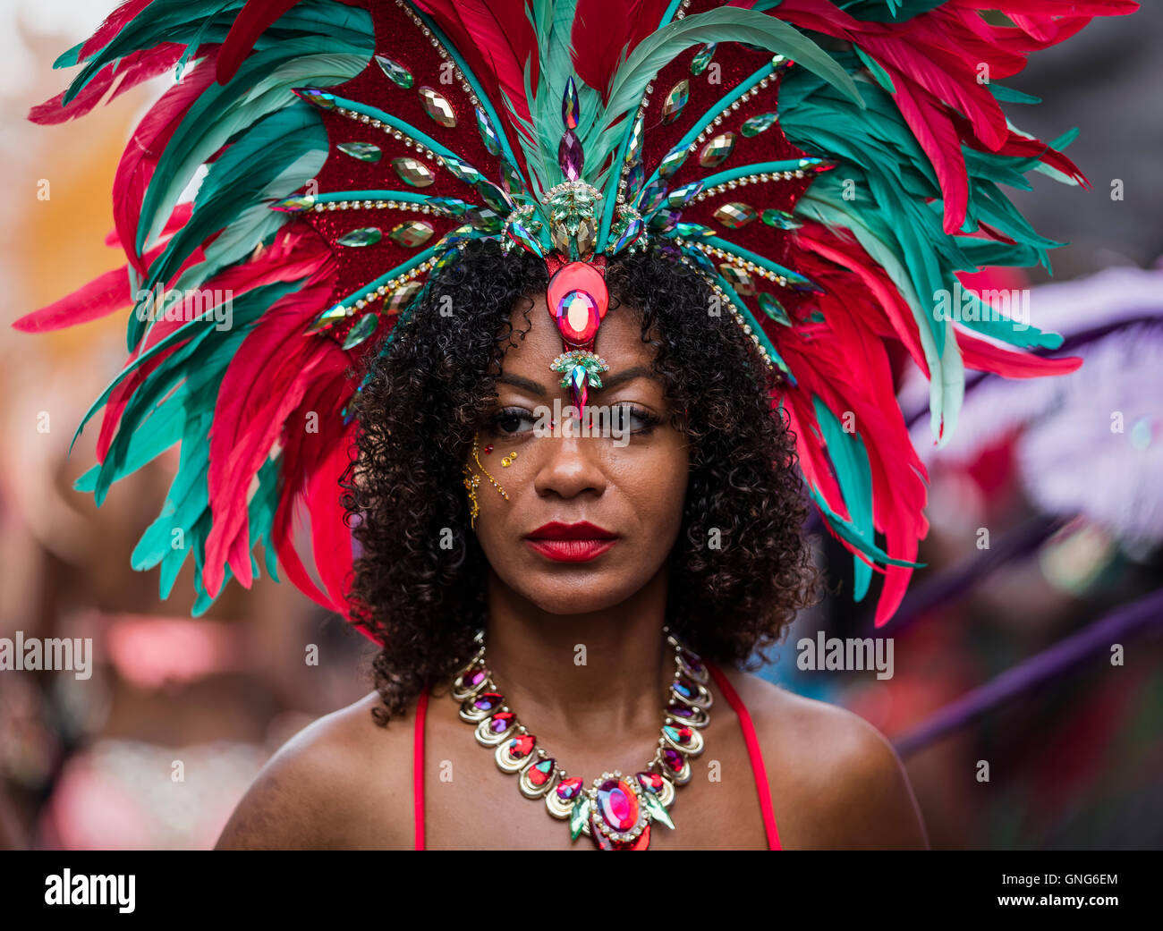 Très jolie dame noire avec le rouge à lèvres rouge et rouge et vert costume de plumes au carnaval de Notting Hill dans l'ouest de Londres Banque D'Images