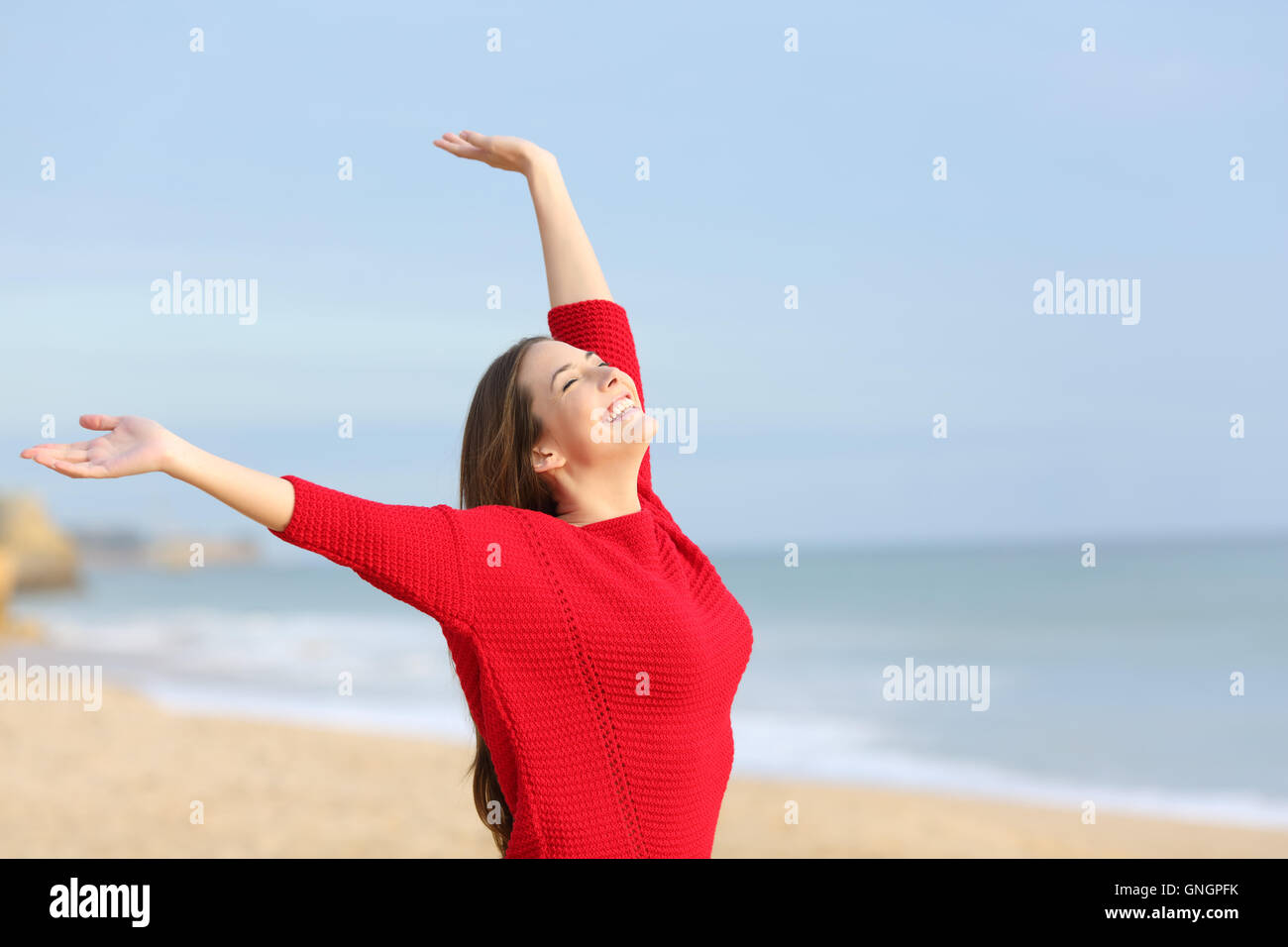 Portrait d'une femme joyeuse heureux excité et raising arms portant un chandail rouge à la plage dans un matin ensoleillé Banque D'Images
