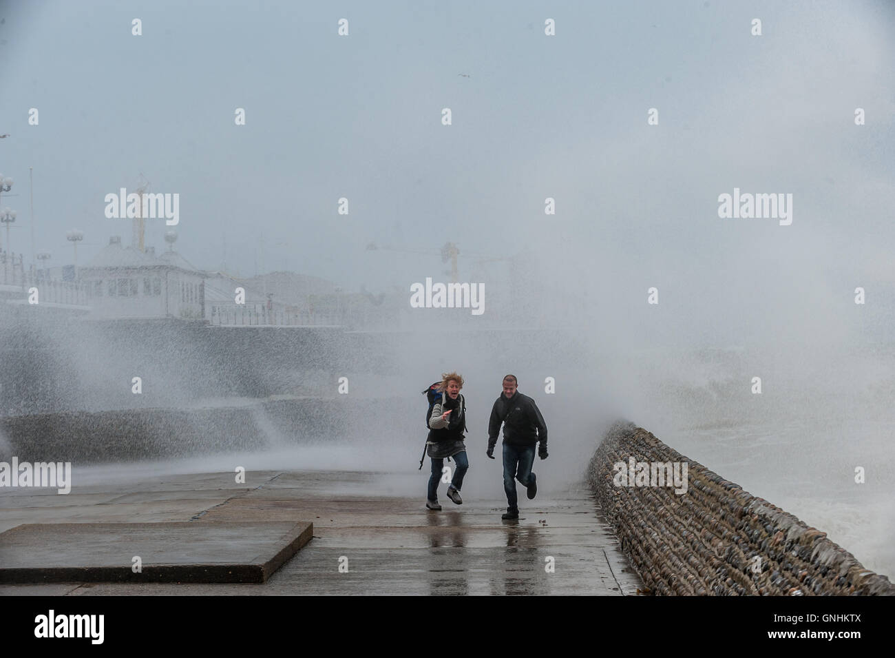 Un couple courir pour échapper aux vagues sur le front de mer à Brighton Banque D'Images