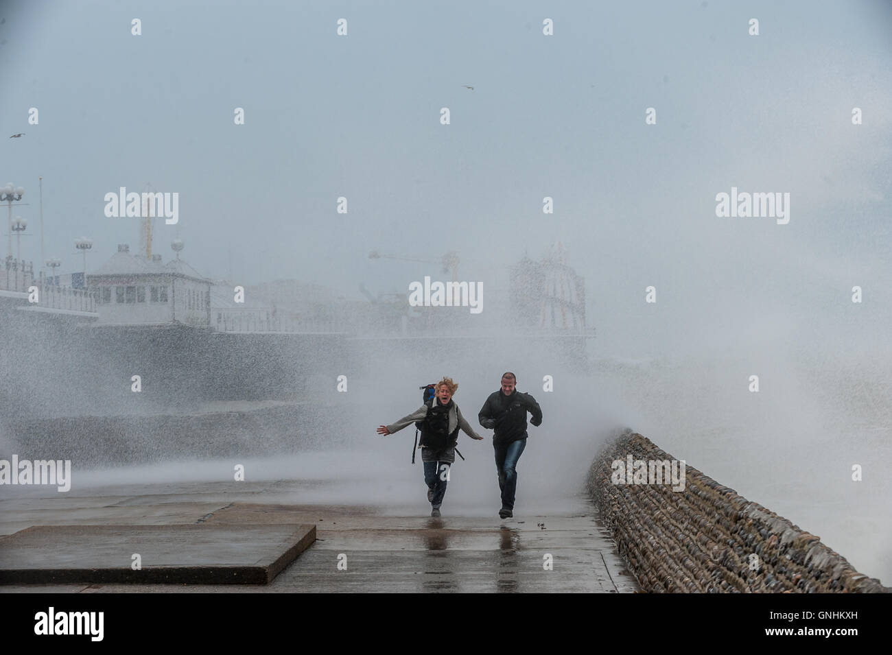 Un couple courir pour échapper aux vagues sur le front de mer à Brighton Banque D'Images