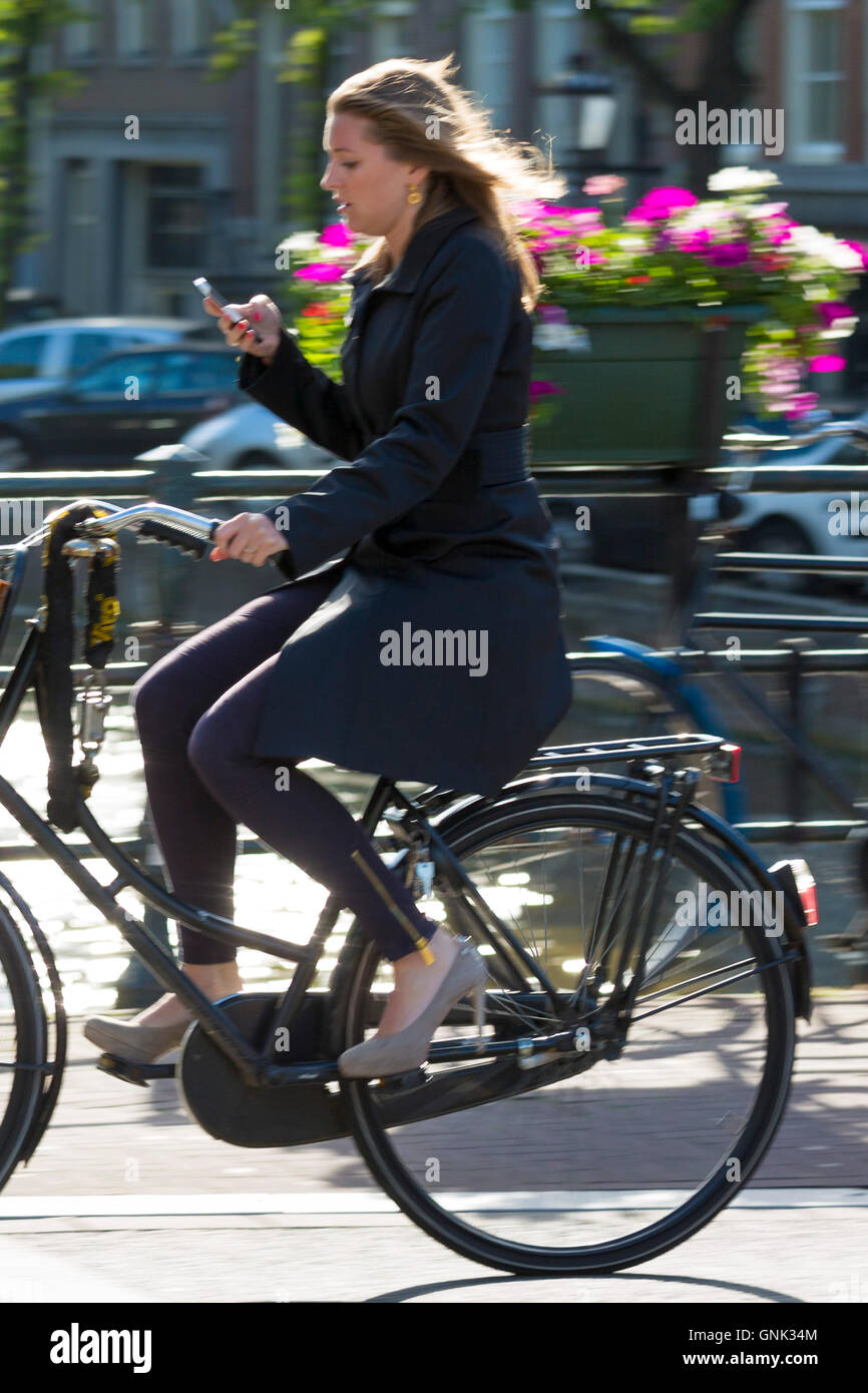 Jeune femme portant des talons hauts chaussures, exerçant son iPhone Cycling out pour la soirée au bridge à Amsterdam, Hollande Banque D'Images