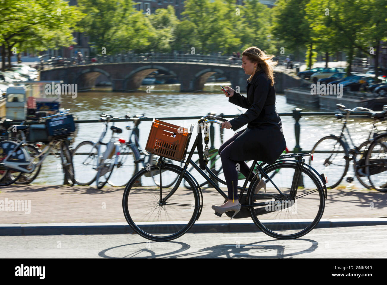 Jeune femme portant des talons hauts chaussures, exerçant son iPhone Cycling out pour la soirée au bridge à Amsterdam, Hollande Banque D'Images