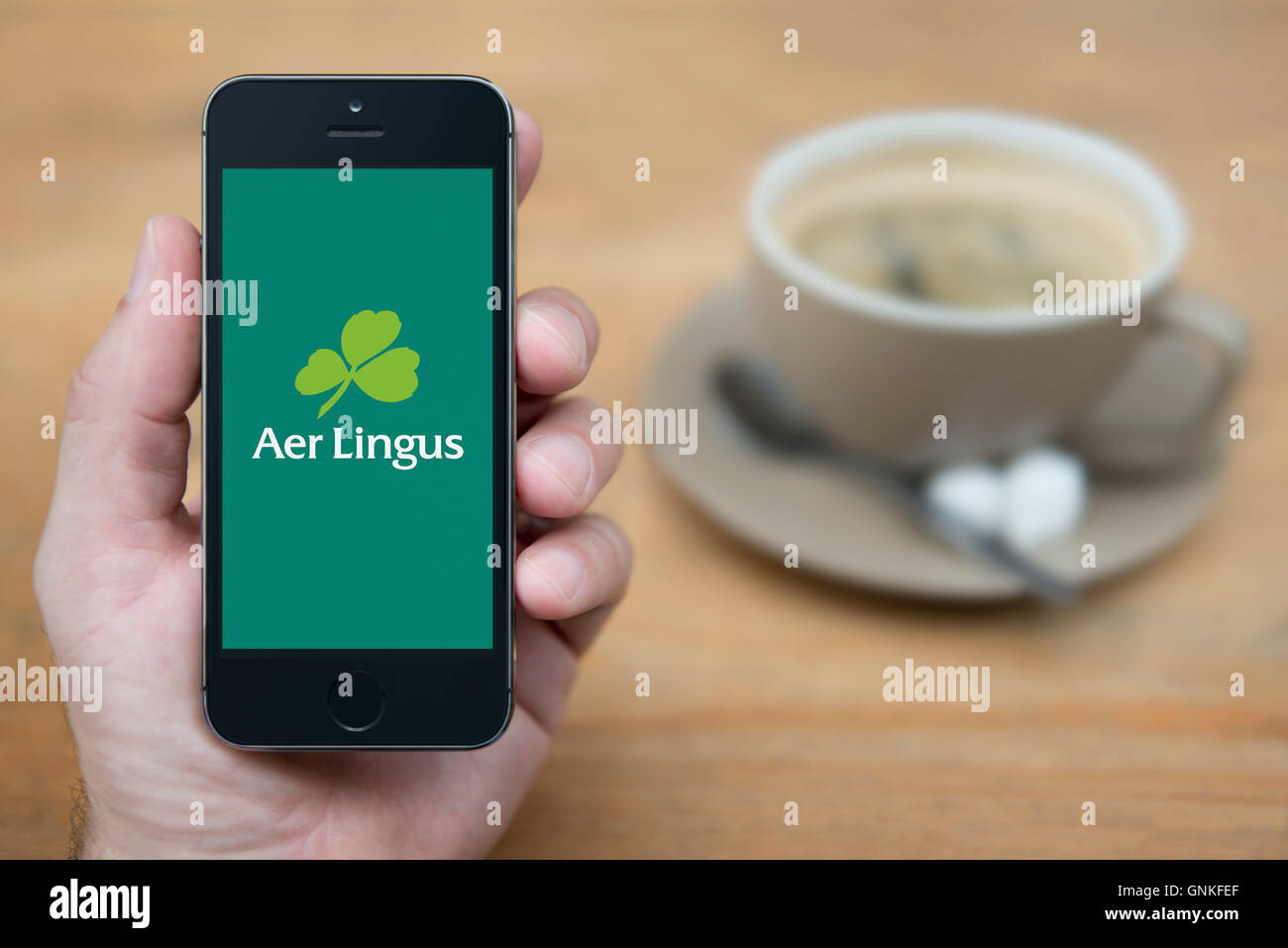 Un homme se penche sur son iPhone qui affiche le logo d'Aer Lingus, tandis qu'assis avec une tasse de café (usage éditorial uniquement). Banque D'Images