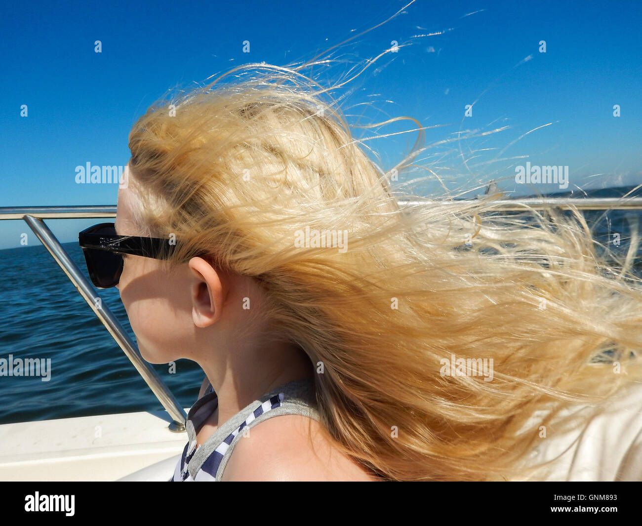 L'enfant blonde sur un bateau avec les cheveux au vent avec ciel bleu clair Banque D'Images