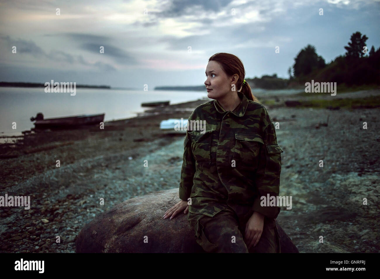 Femme randonneur en vêtements de camouflage en assis sur la rive de la rivière à pierre Banque D'Images