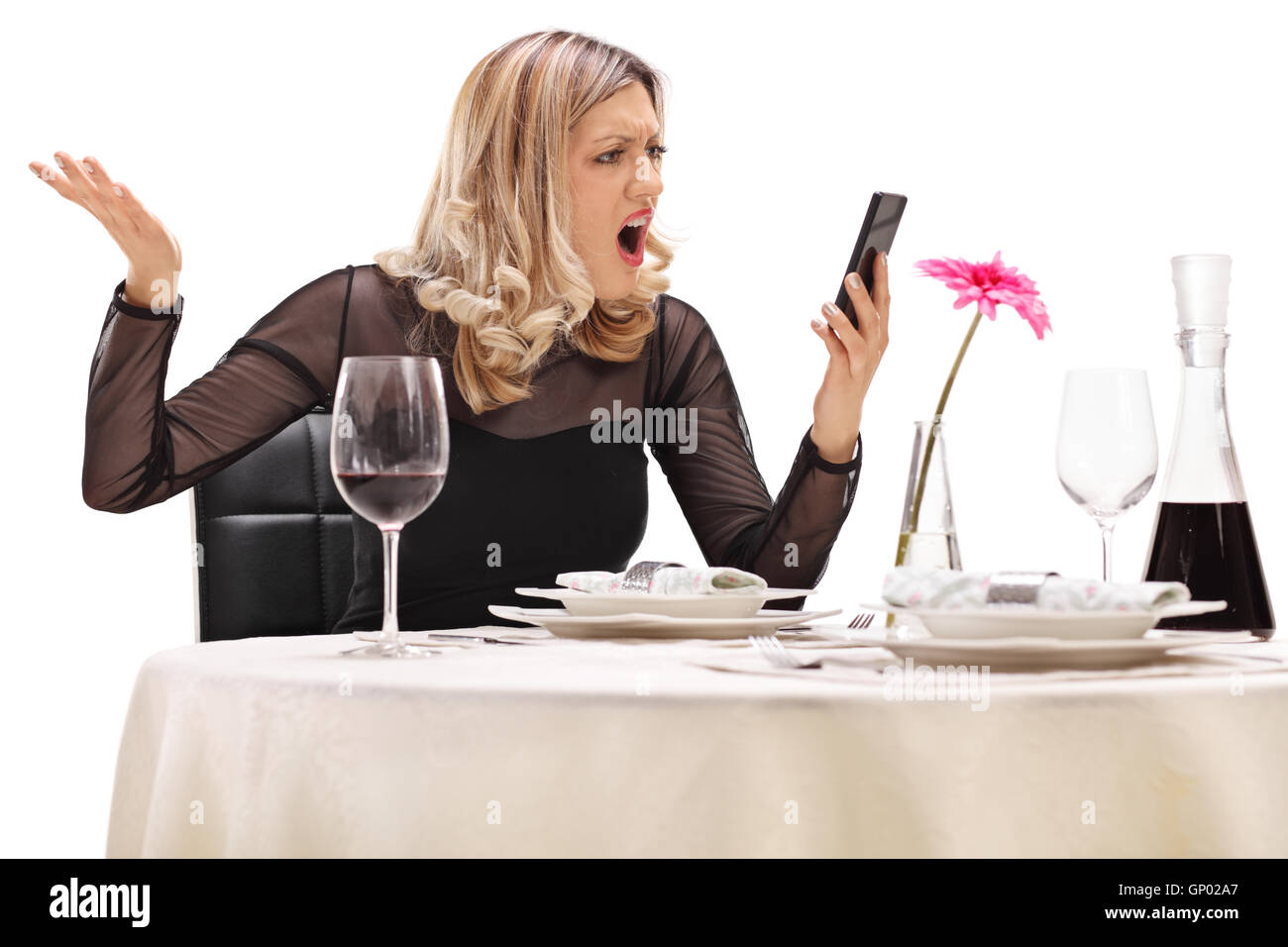 Furieux femme assise à une table de restaurant et de la lecture d'un message sur son téléphone isolé sur fond blanc Banque D'Images