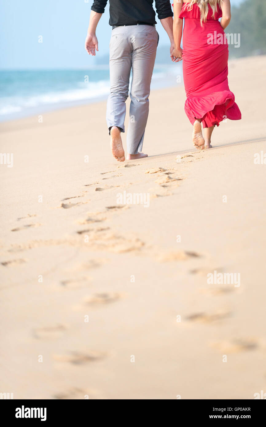 Couple en train de marcher sur la plage avec des empreintes sur le sable. Copier l