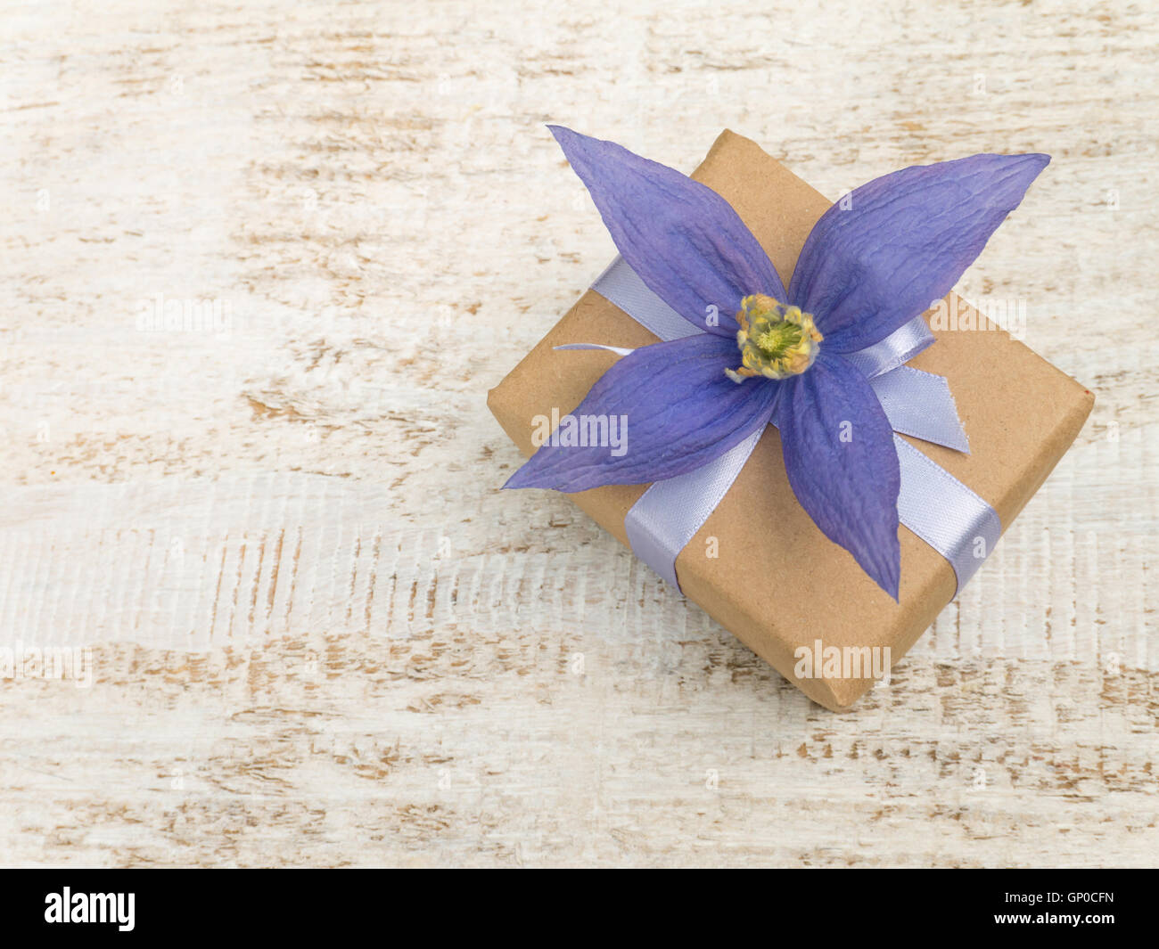 Boîte-cadeau enveloppé dans du papier kraft brun avec ruban en satin et quatre pétales violet fleur sur le bord en bois peint blanc Banque D'Images