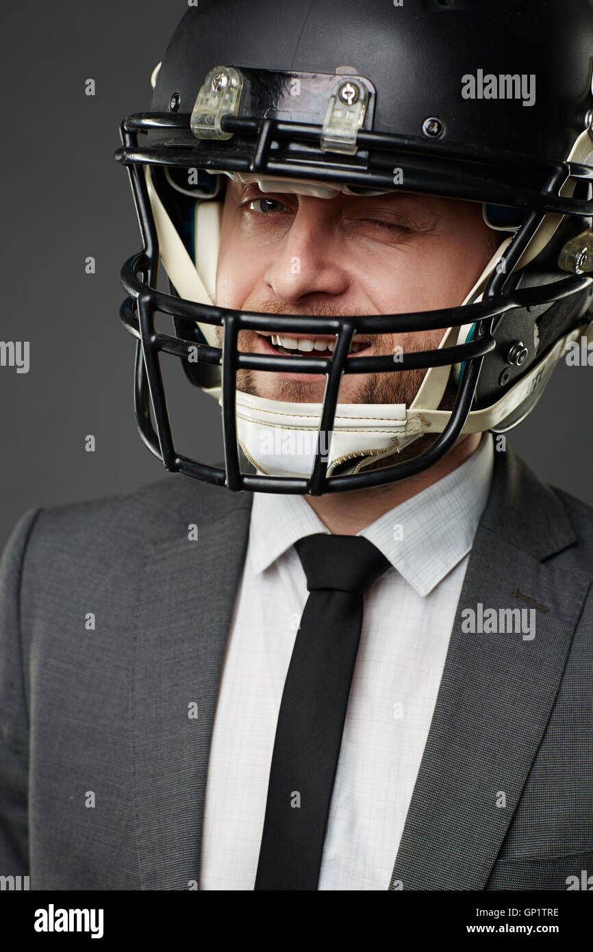 Portrait of smiling businessman wearing costume et American football helmet camera, des clins d'œil isolé sur fond noir. Banque D'Images