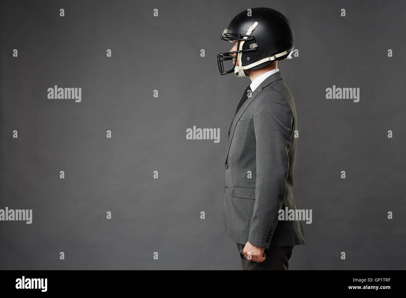 Weda de businessman wearing costume sur mesure et American football helmet avec confiance permanent orienté vers la gauche, isolated on black b Banque D'Images