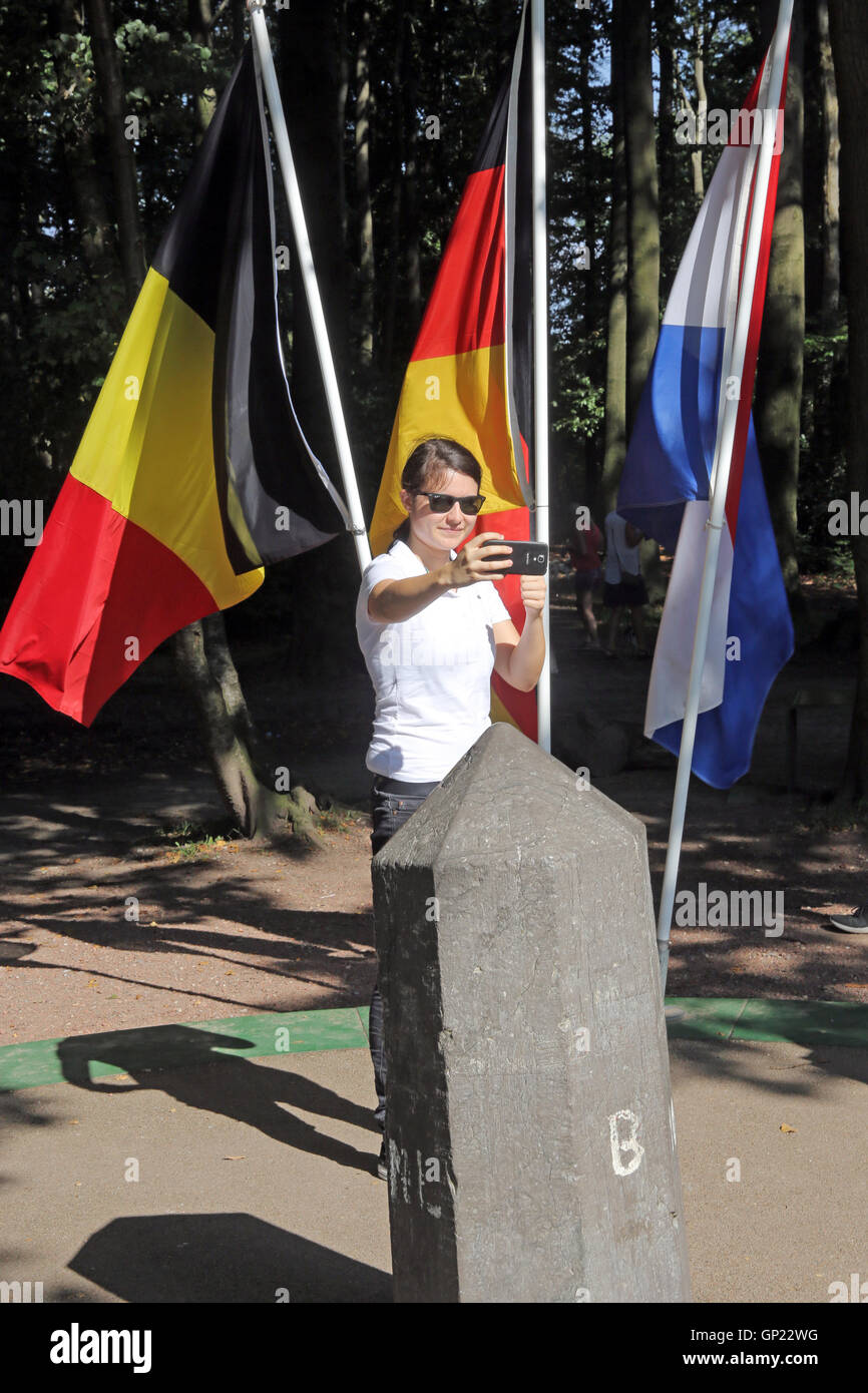 Femme prend une photo d'elle-même avec les drapeaux de Belgique, Allemagne, Pays-Bas et en face de la boarder-pierre sur le point "reilaendereck' près de Aix-la-Chapelle, où les frontières de l'Allemagne, Pays-Bas et Belgique. Cet endroit est le point le plus élevé (322 mètres) des Pays-Bas. Banque D'Images