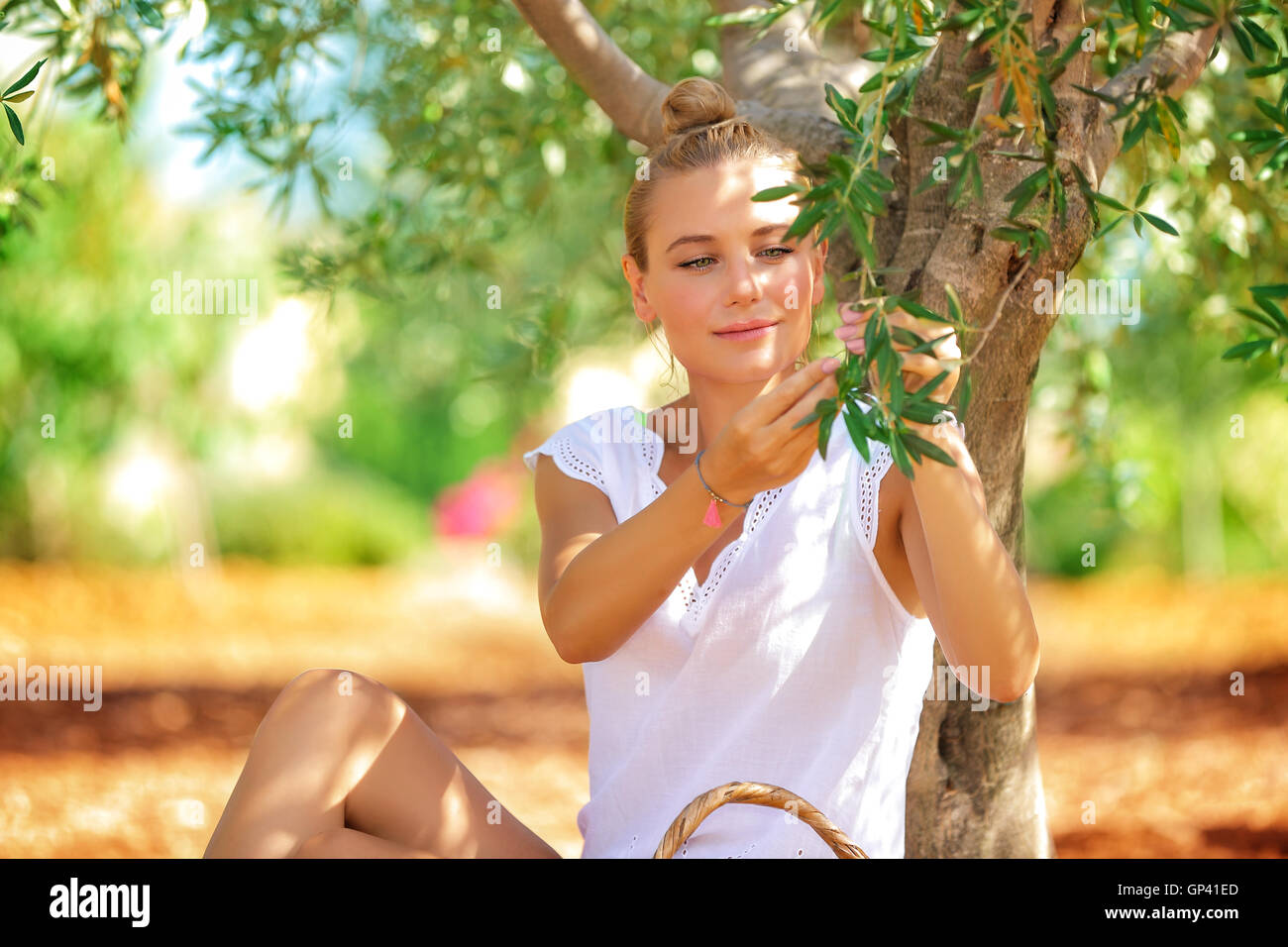 Belle femme blonde assise dans le jardin près de l'olivier et la cueillette de petits fruits vert peu, profiter de la vie à la campagne Banque D'Images