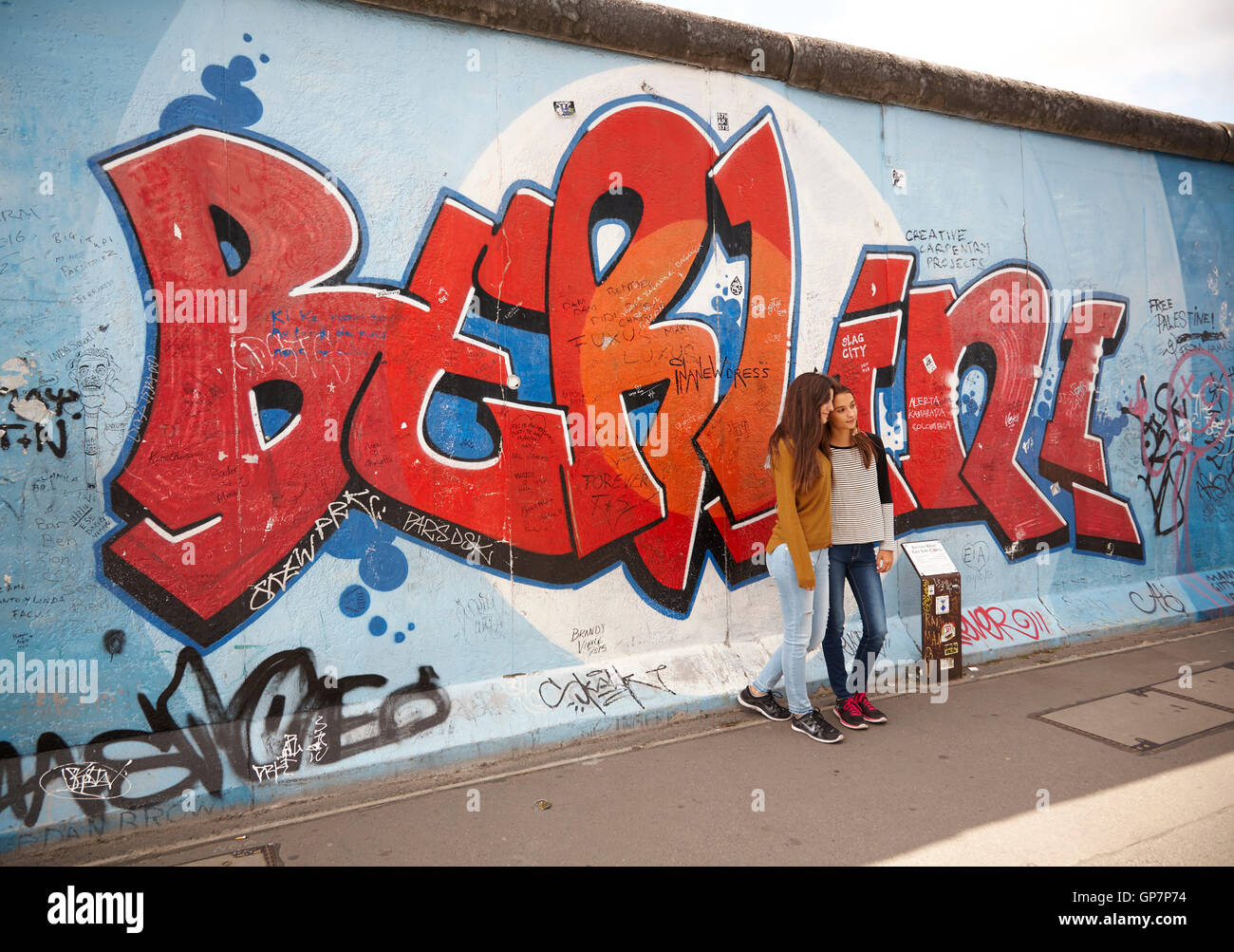 Deux jeunes dames posant par la peinture de Berlin à l'East Side Gallery du mur de Berlin en Allemagne. Banque D'Images