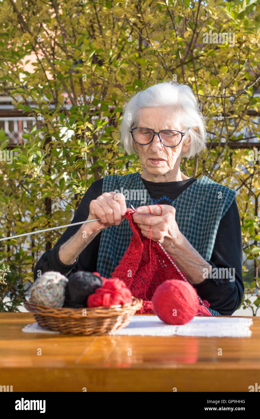 Senior woman knitting avec laine rouge à l'extérieur Banque D'Images