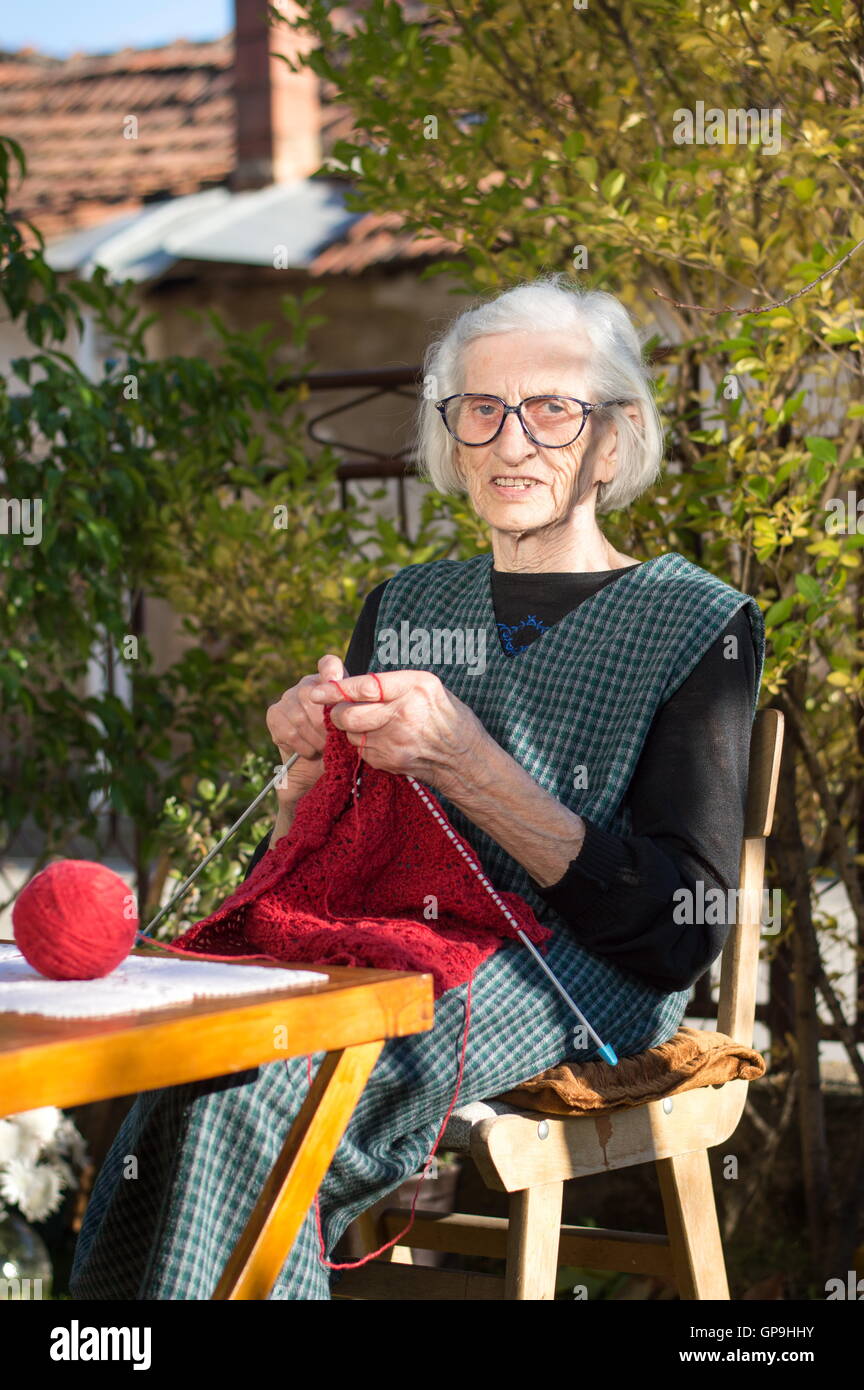 Senior woman knitting avec laine rouge à l'extérieur Banque D'Images