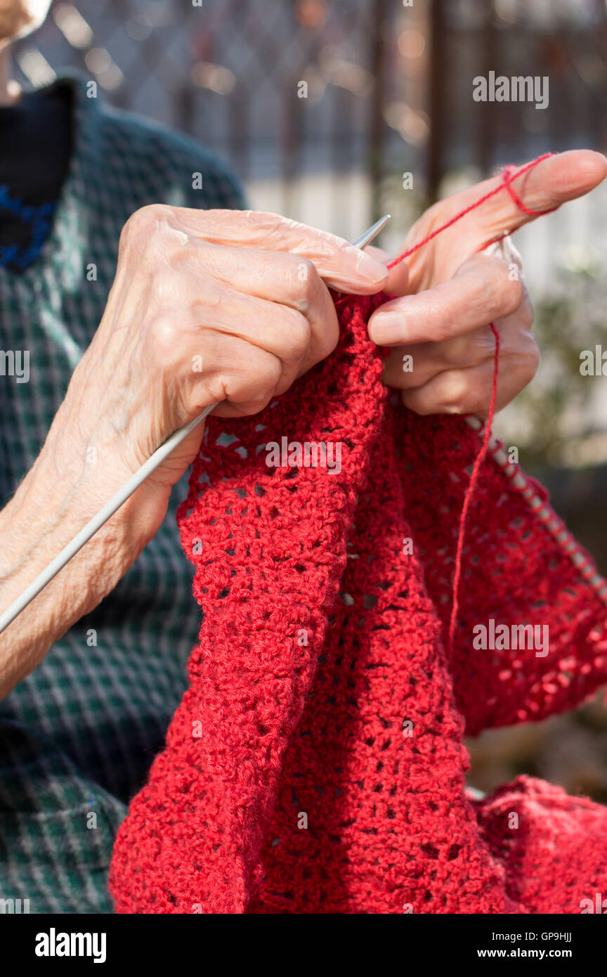 Senior woman knitting mains avec de la laine rouge à l'extérieur Banque D'Images
