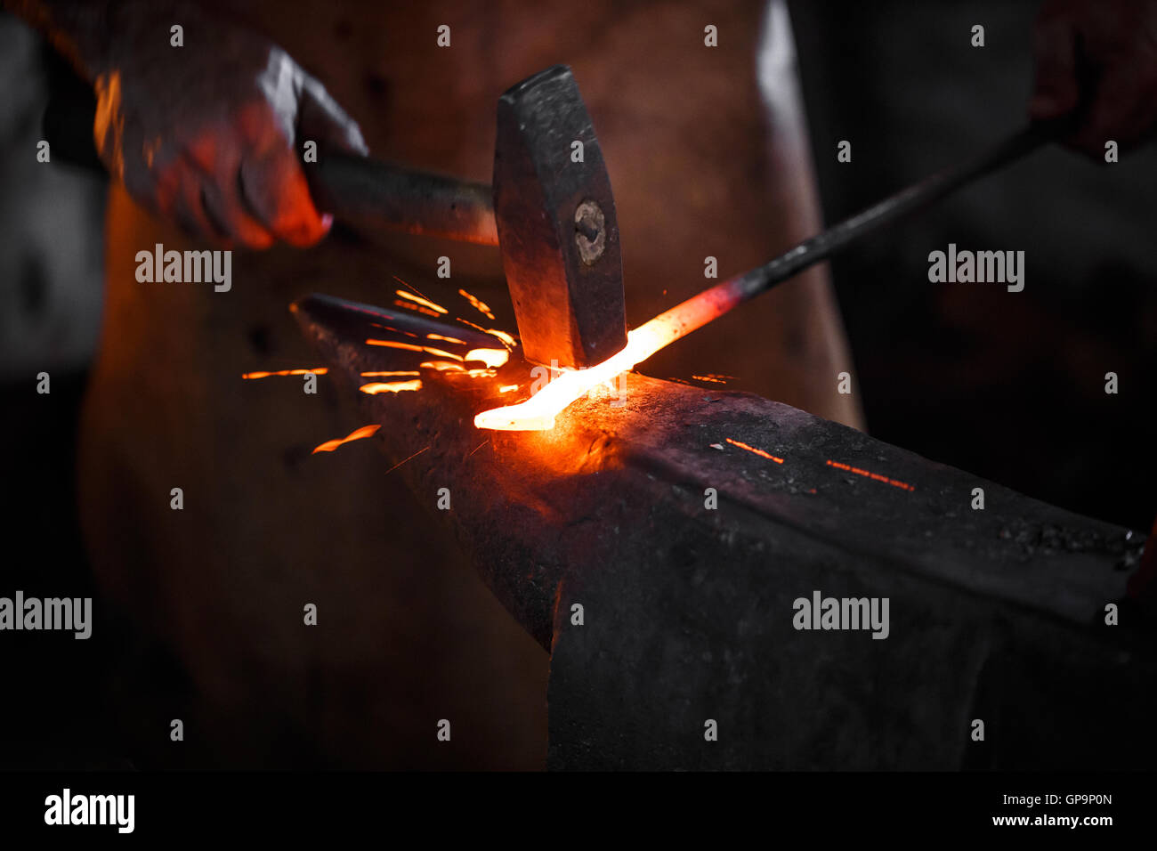 Le forgeron forge manuellement le métal en fusion sur l'enclume dans la forge d'artifice d'étincelles Banque D'Images