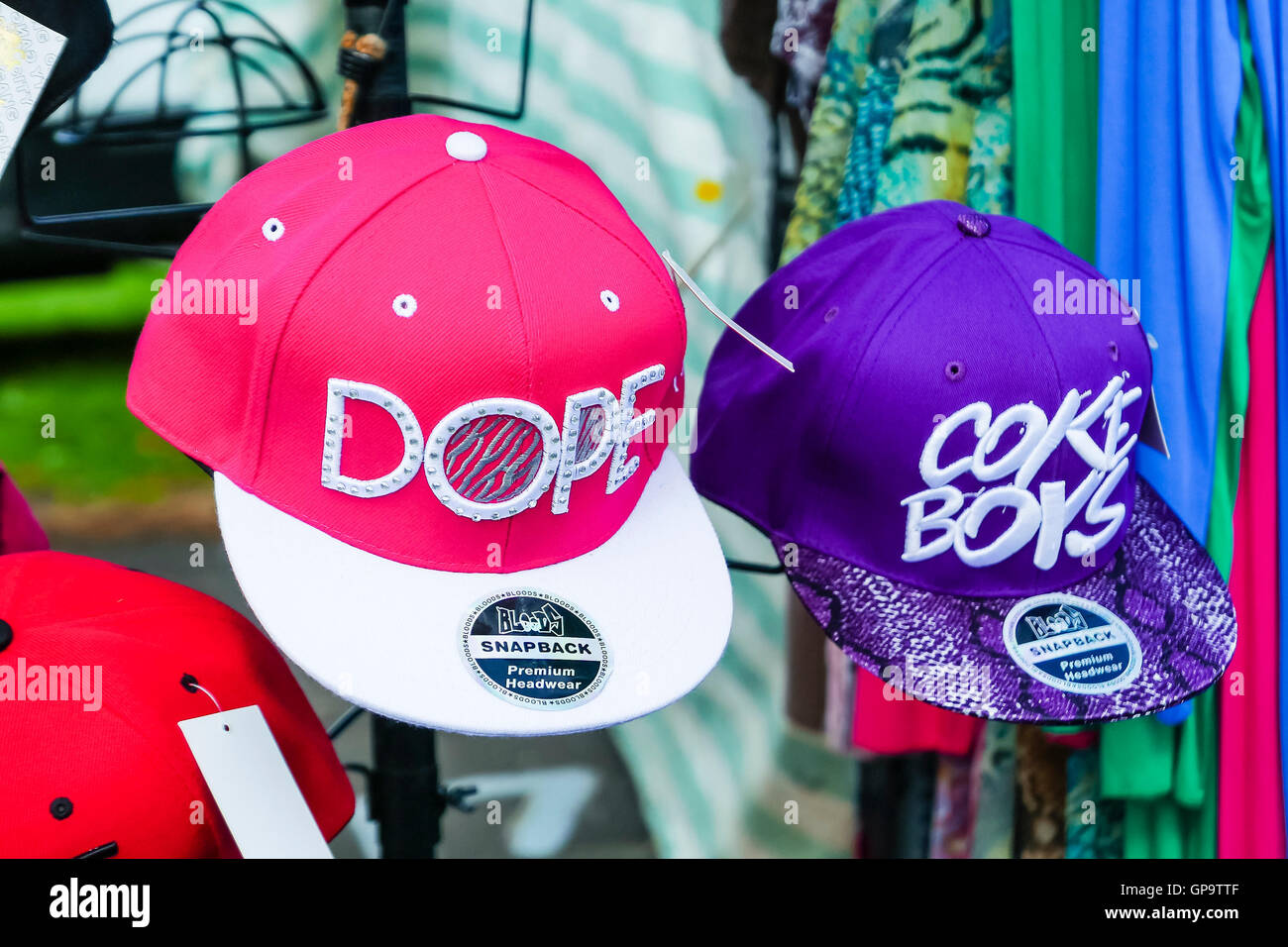 Rose et violet casquettes de baseball avec des slogans 'Dope' et 'Boys' Coke en vente sur un étal de marché. Banque D'Images
