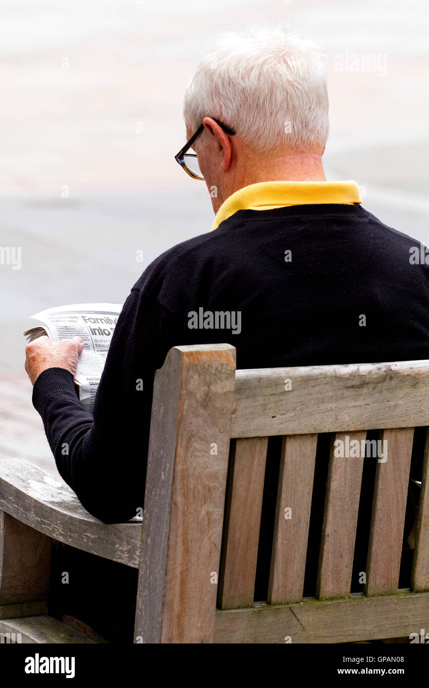 Un homme âgé assis sur un siège d'été de lire le journal dans le centre de Dundee, Royaume-Uni Banque D'Images